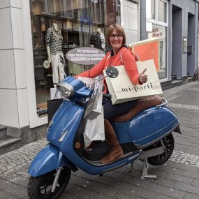 glückliche Kundin eines E-Rollers von Kumpan electric mit Einkaufstüten in den Innenstadt